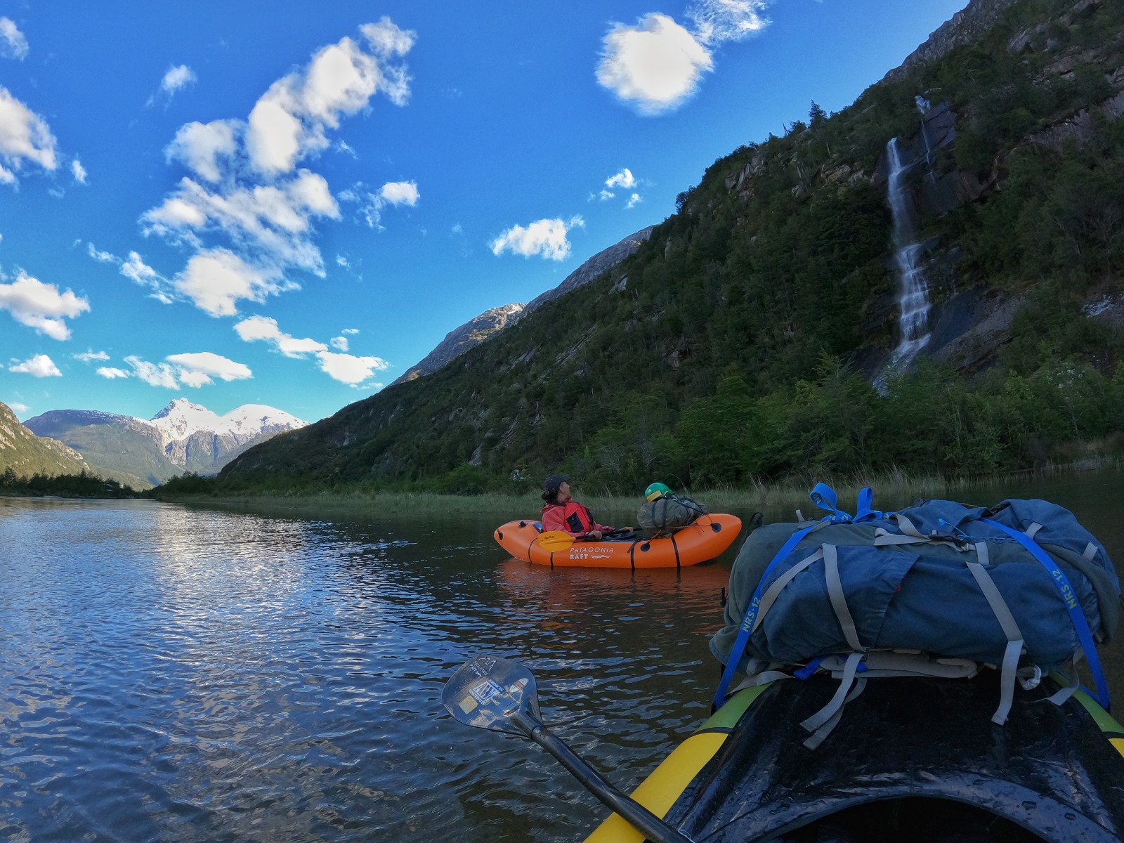Packraft junto a una cascada que cae por el acantilado