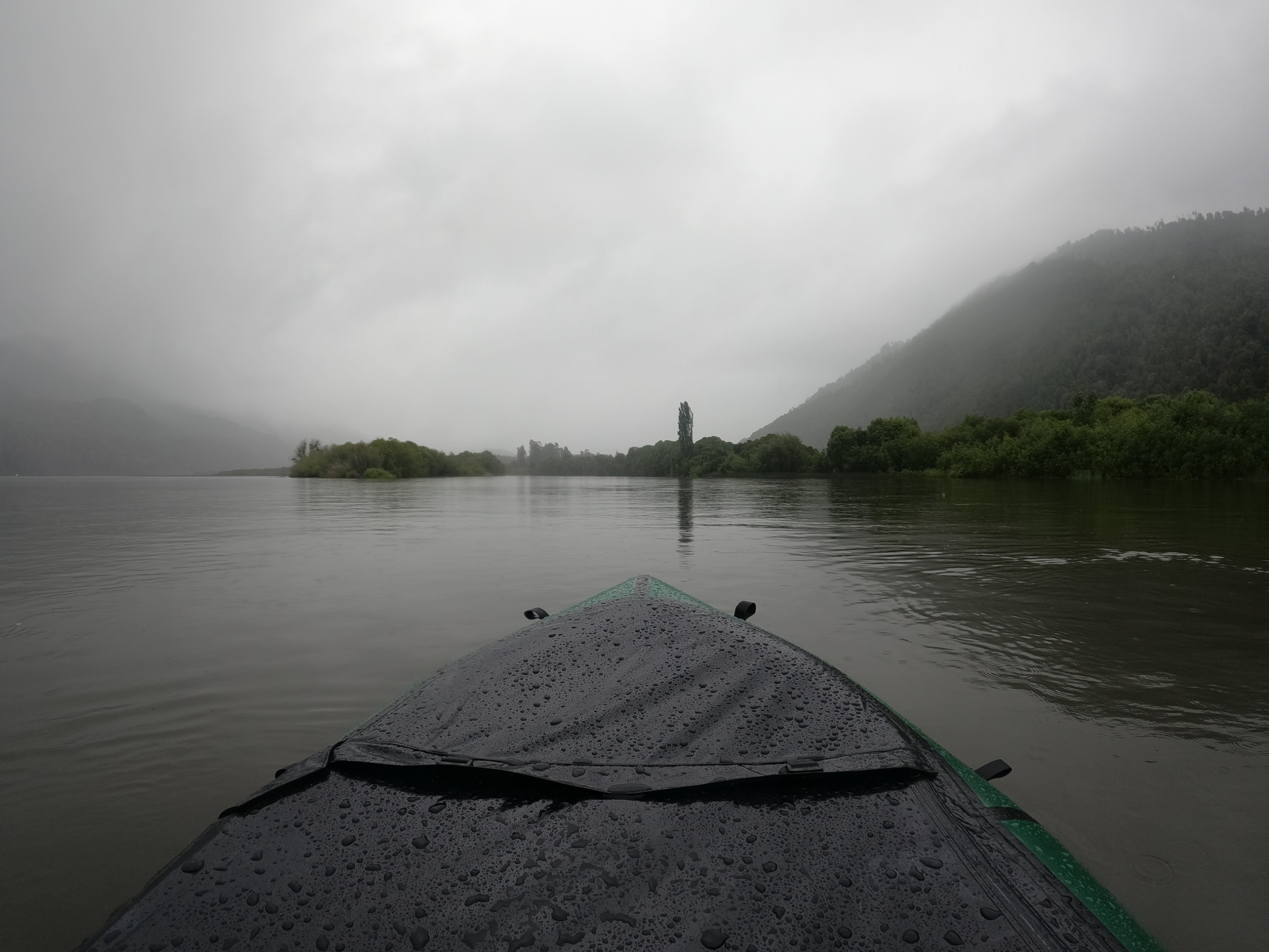 Proa del bote sobre agua calma con niebla en los cerros